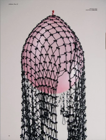Stylized close-up of a pink balloon covered in black beaded netting and photographed against a light grey seamless backdrop.