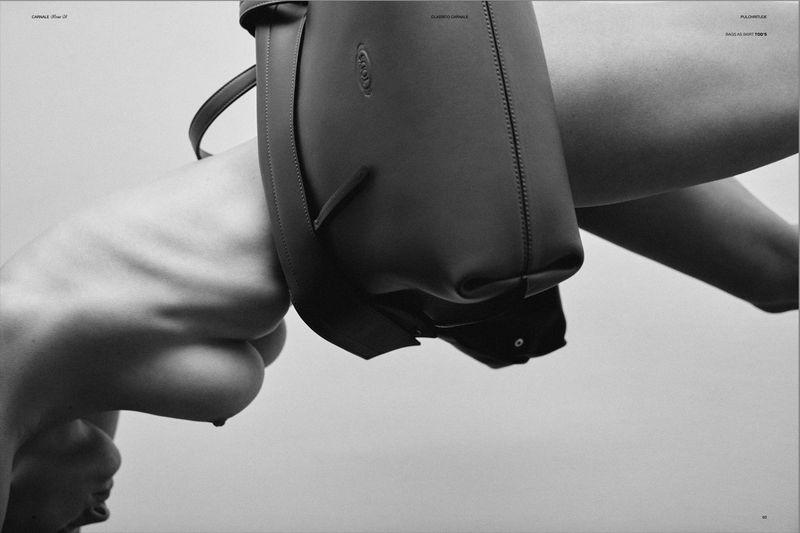 Monochromatic studio shot of a black leather tote bag hanging near a woman's torso against a neutral backdrop in a fashion editorial.