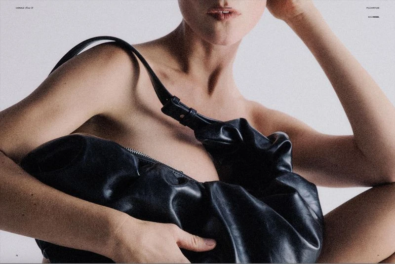 Close-up fashion shot featuring an adult woman with fair skin holding a black leather bag against a plain white background.
