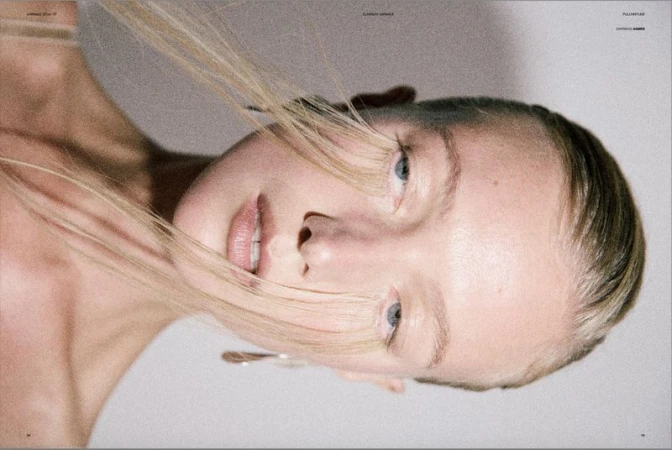 Model Lou Schoof in an intimate close-up beauty portrait with strands of blonde hair draped across her eyes against a neutral backdrop.
