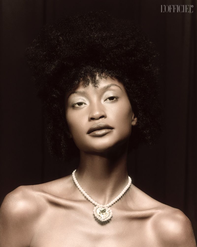 Glamorous portrait of an African-American woman with afro hairstyle wearing an elaborate pearl necklace against a dark studio backdrop.