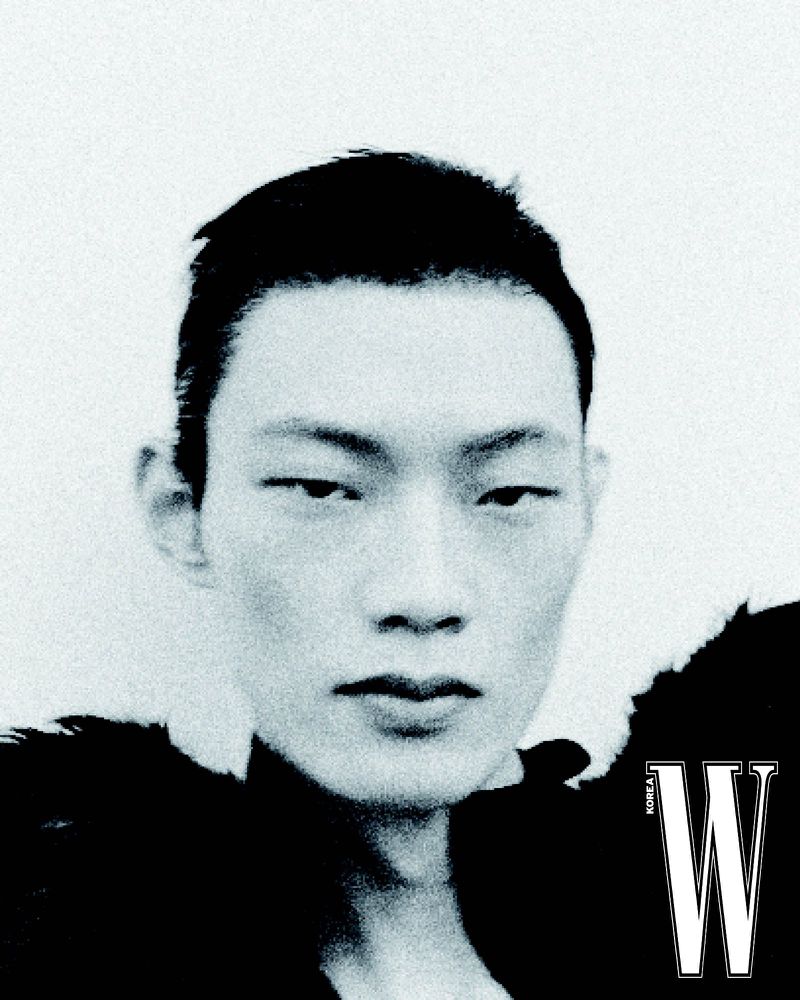 Close-up black and white portrait of model Hoyong Kim wearing a black textured collar against a white backdrop for W Korea.