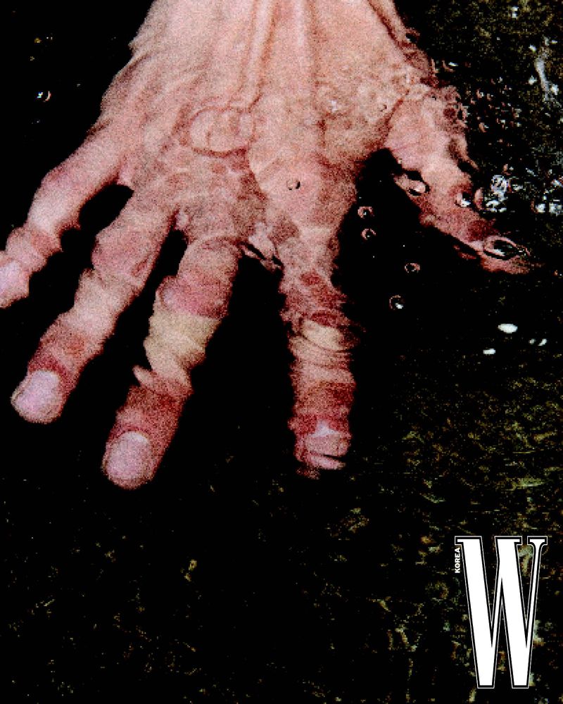 Close-up image of a person's hand under water, creating a distorted and reflective effect, against a dark, textured background.
