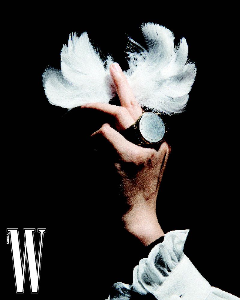 Elegant fashion photo featuring a hand adorned with a large ring and delicate white feathers against a stark black background.