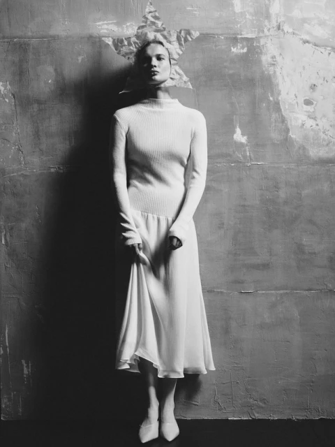 Monochrome portrait of a young adult woman wearing a white dress and star-shaped headpiece against a textured studio backdrop.
