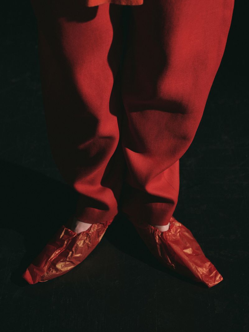Close-up of human legs and feet wearing red trousers and red shoe covers, set against a dark backdrop in a studio photograph.