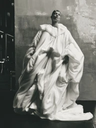 Model wearing an oversized voluminous white quilted cocoon gown standing against a textured studio wall.