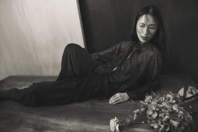 Monochrome shot of a woman reclining on a wooden surface in a striped blouse and trousers beside dried flowers.