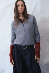 Model Waleska Gorczevski wearing a grey collared sweater and pleated navy trousers against a crinkled white paper backdrop.