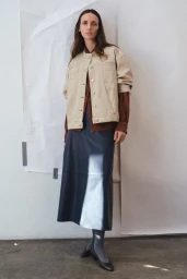Model Waleska Gorczevski wearing a beige jacket and dark skirt against a white studio background for TWP Pre-Fall 2026.