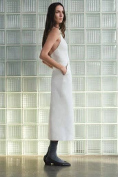 Model Waleska Gorczevski in profile wearing a white halter midi dress and grey socks in front of a glass block wall.