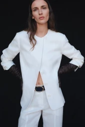 Model Waleska Gorczevski wearing a white jacket and trousers with dark leather gloves against a black background for TWP Pre-Fall 2026.
