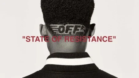 Rear view of a black man with the Off-White logo shaved into his short hair, wearing a black jacket against a plain white background.