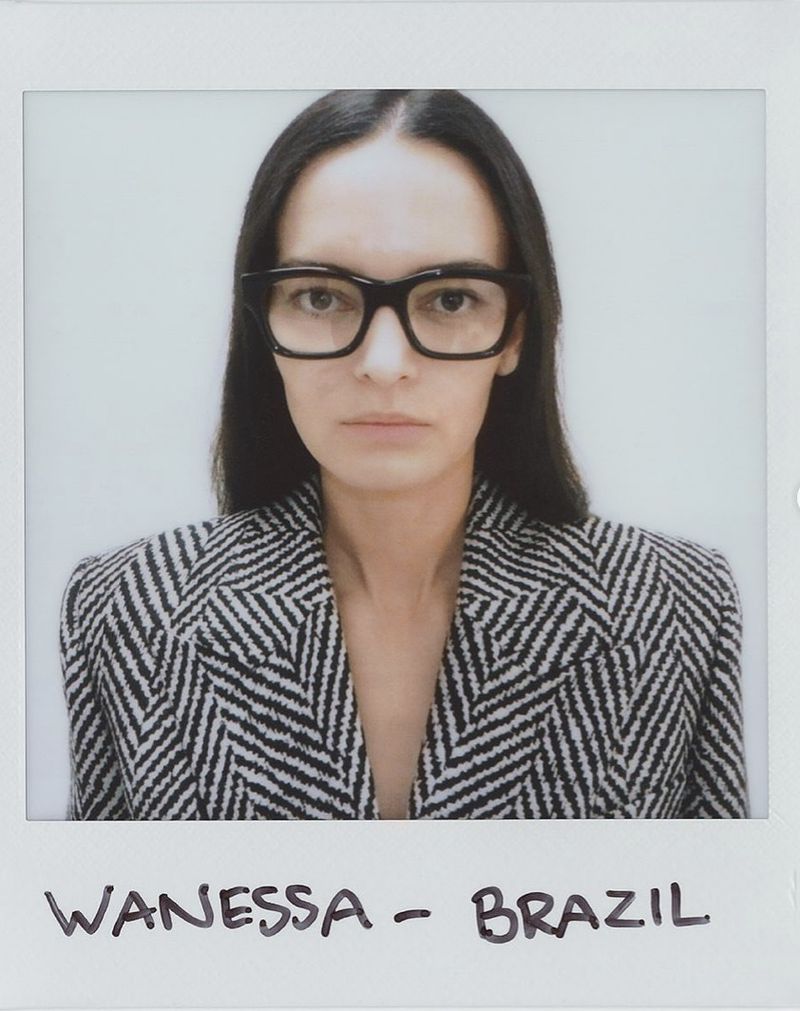 Polaroid photograph of a model wearing black-rimmed glasses and a black and white patterned blazer against a white background.