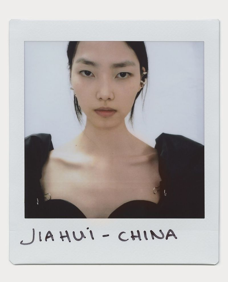Close-up portrait of a young Asian woman with black hair and a black dress. The photo is in a polaroid frame.