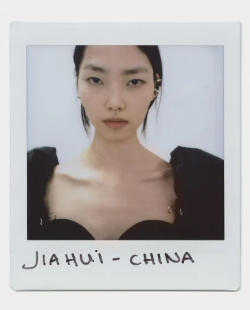 Close-up portrait of a young Asian woman with black hair and a black dress. The photo is in a polaroid frame.