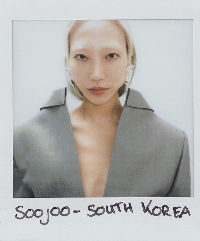 Polaroid-style portrait of a South Korean woman with platinum blonde hair, wearing a grey blazer, and statement earrings.