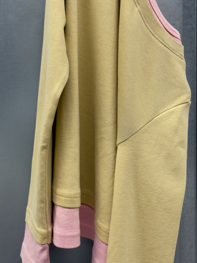 Close-up shot of a light yellow long-sleeved shirt layered over a pink shirt. The soft, muted colors and simple design create a minimalist aesthetic.