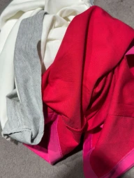 Piled layers of folded colourful garments including red, pink, white, and grey fabrics.