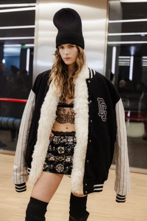 Fashionable woman in a black bomber jacket, sequined skirt, and knit beanie poses indoors; chic urban style, confident pose, and trendy fashion.