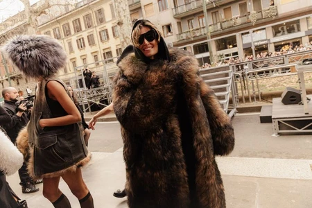 Model wearing a large brown fur coat and black sunglasses outdoors on a city street during Dolce and Gabbana fashion project