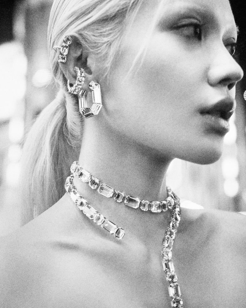 Close-up monochrome portrait of a woman wearing crystal ear cuffs, hoop earrings, and a layered crystal necklace for Swarovski.