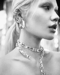 Close-up monochrome portrait of a woman wearing crystal ear cuffs, hoop earrings, and a layered crystal necklace for Swarovski.