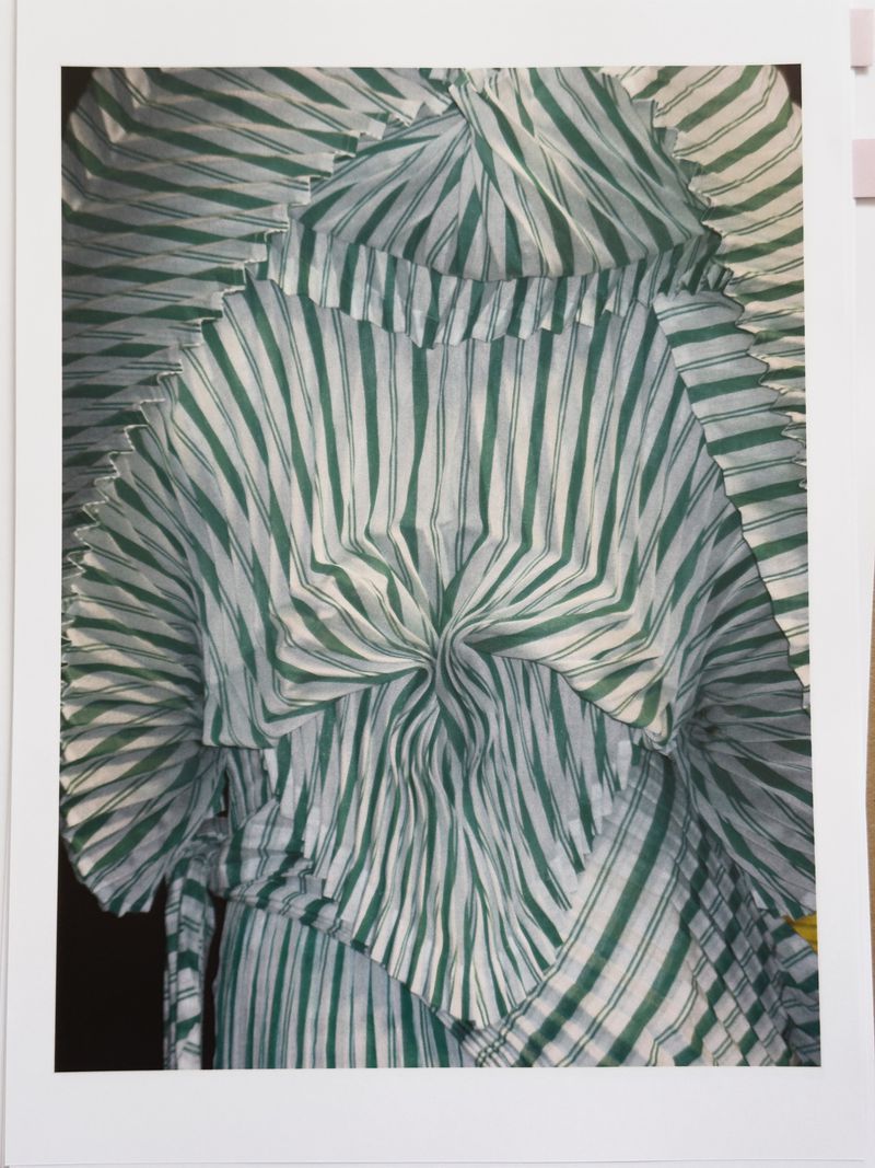 Close-up of a white fabric garment with green vertical stripes and radial pleats, forming a textured pattern, suitable for fashion context.
