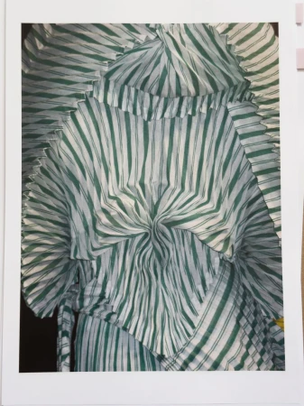Close-up of a white fabric garment with green vertical stripes and radial pleats, forming a textured pattern, suitable for fashion context.