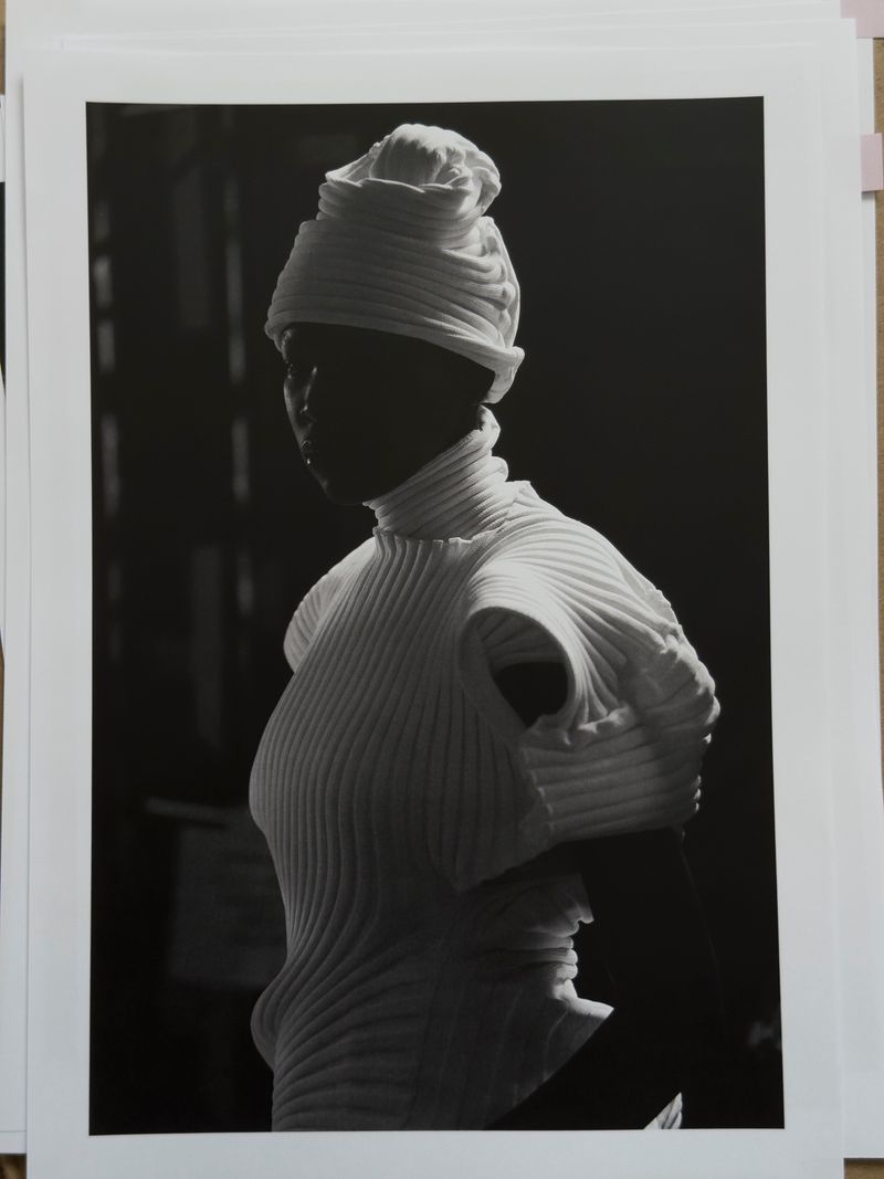Model wearing white pleated top and matching headwrap in high contrast lighting for Issey Miyake x Byredo