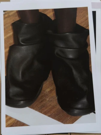 Close-up studio shot of black leather booties with brown leggings on a wood background, presented on white cards with a light grey border.