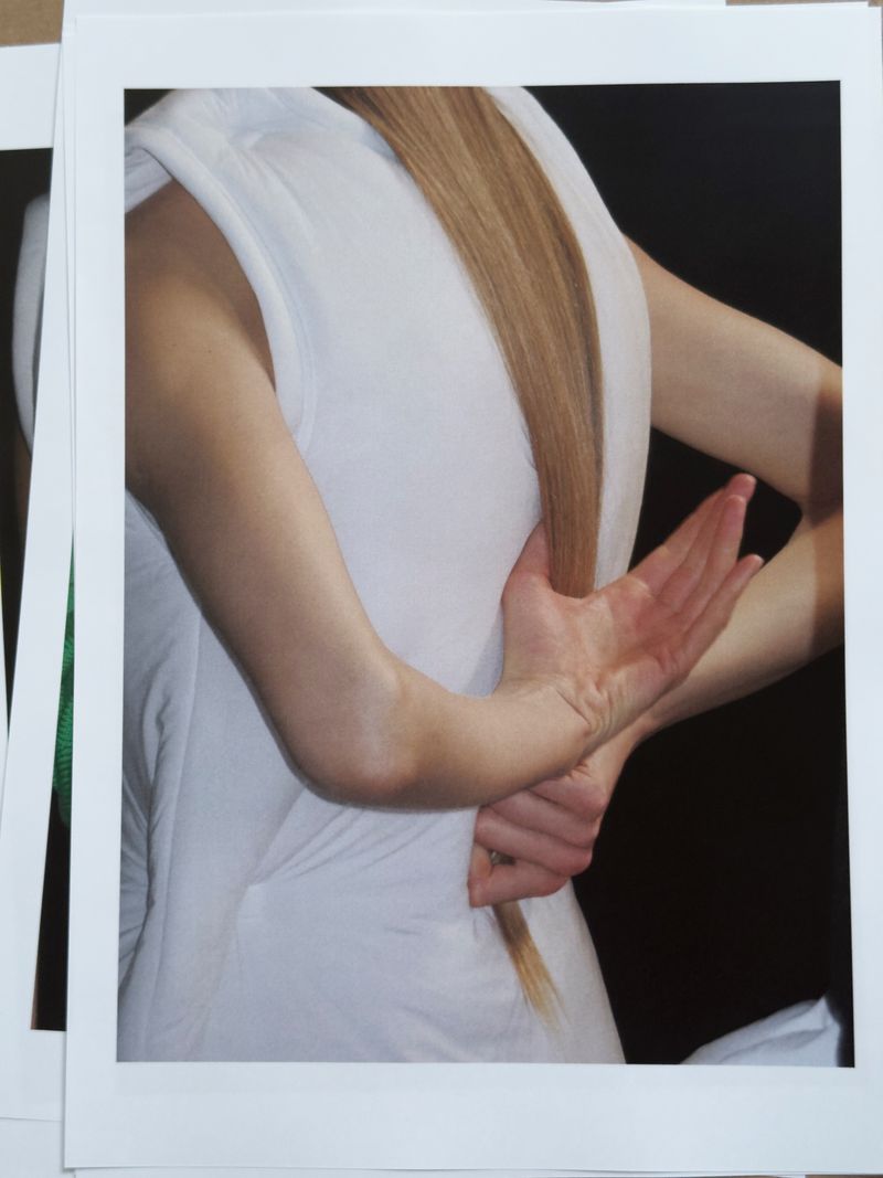 Woman with light brown hair and a white dress is shown from behind. The woman has her arms crossed behind her back.