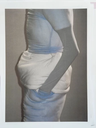 Monochromatic art photograph features a person draped in light blue and white fabric, with an arm bent across their body. 