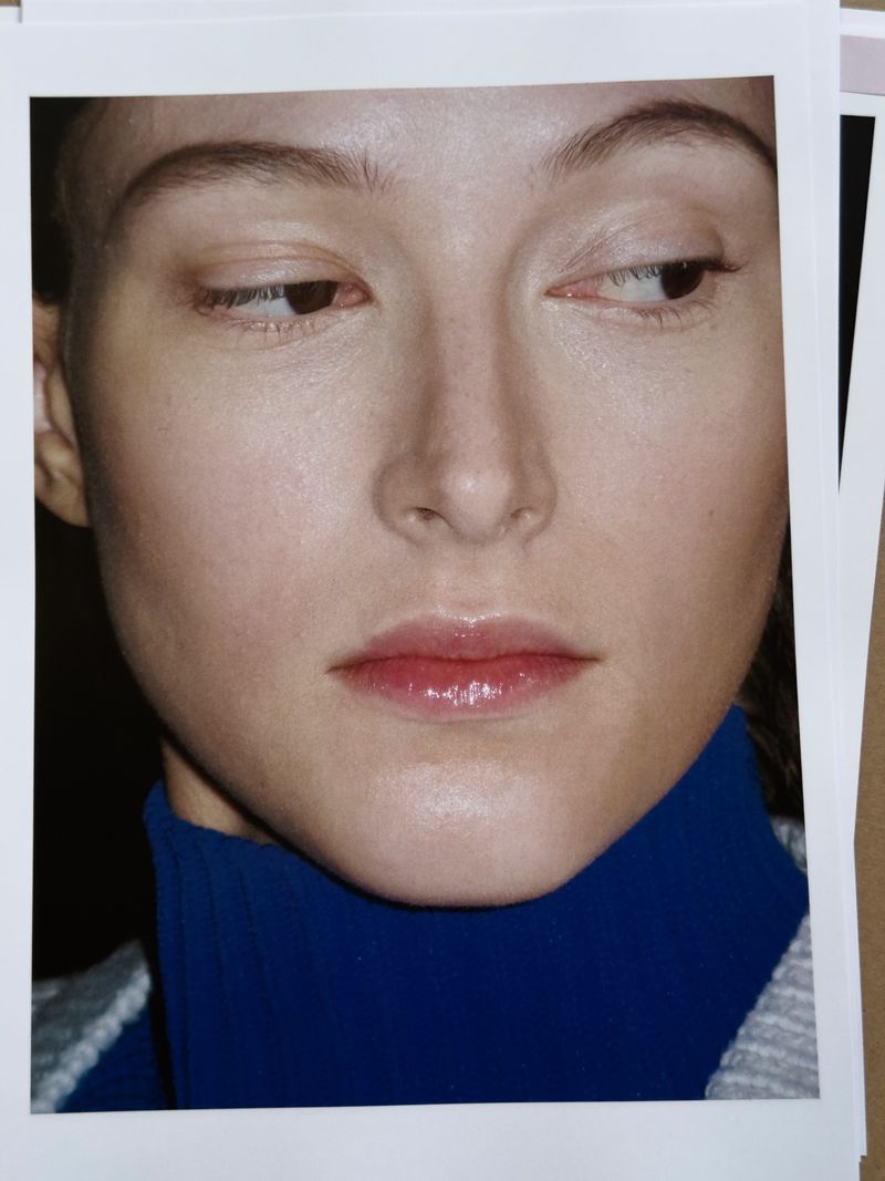 Close-up portrait of a fair-skinned woman with a neutral expression, wearing a blue turtleneck, captured in a brightly lit photo studio.