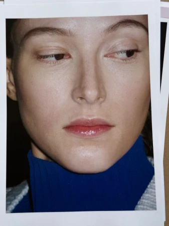 Close-up portrait of a fair-skinned woman with a neutral expression, wearing a blue turtleneck, captured in a brightly lit photo studio.