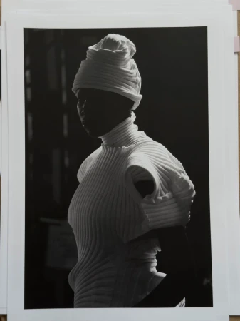 Model wearing white pleated top and matching headwrap in high contrast lighting for Issey Miyake x Byredo