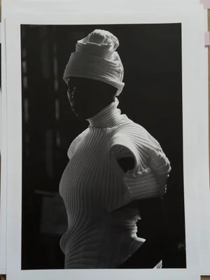 Model wearing white pleated top and matching headwrap in high contrast lighting for Issey Miyake x Byredo