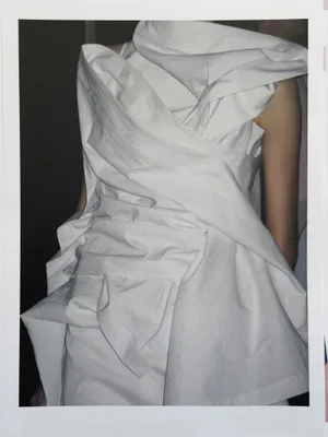 Model wearing a structured white wrapped architectural garment with draped fabric details