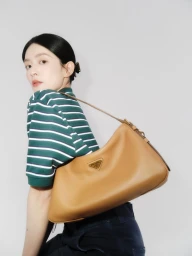Woman wearing a green striped top carrying a tan leather shoulder bag against a neutral studio background