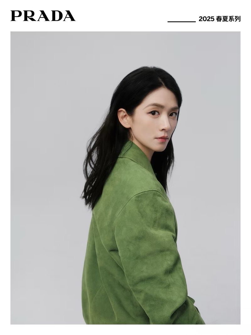 Fashion portrait of a woman with long dark hair wearing a green jacket against a gray background, featuring Prada branding and a 2025 spring collection title.