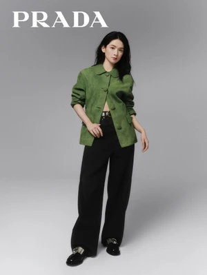 Amy Chen Haoyu wearing a green jacket and black trousers against a neutral grey studio backdrop for Prada