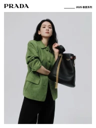 Woman in green jacket holding a black shoulder bag against a neutral studio backdrop