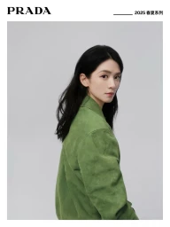 Portrait of an East Asian woman with long dark hair wearing a green jacket against a grey background