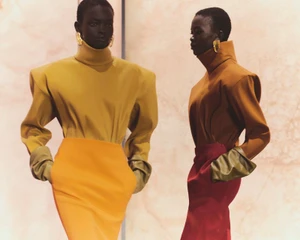 Two models wearing structured turtleneck tops and bold earrings standing against a marble wall for Saint Laurent Winter 25