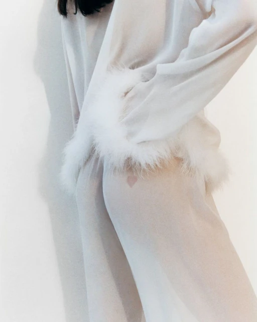 Sheer white robe with feathered cuffs on a woman against a white backdrop. Soft, elegant fashion statement. Beauty and simplicity defined.