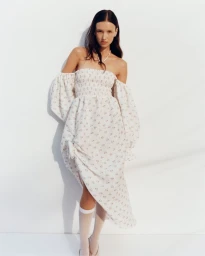 Model in a white off-the-shoulder smocked dress with puff sleeves against a white backdrop for Sleeper S/S 25.