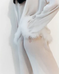 Model wearing a white satin set with feathered cuffs against a plain white studio background for Sleeper S/S 25.