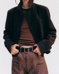 Model wearing a dark brown jacket over a brown top and matching leather trousers with a black belt against a white background.