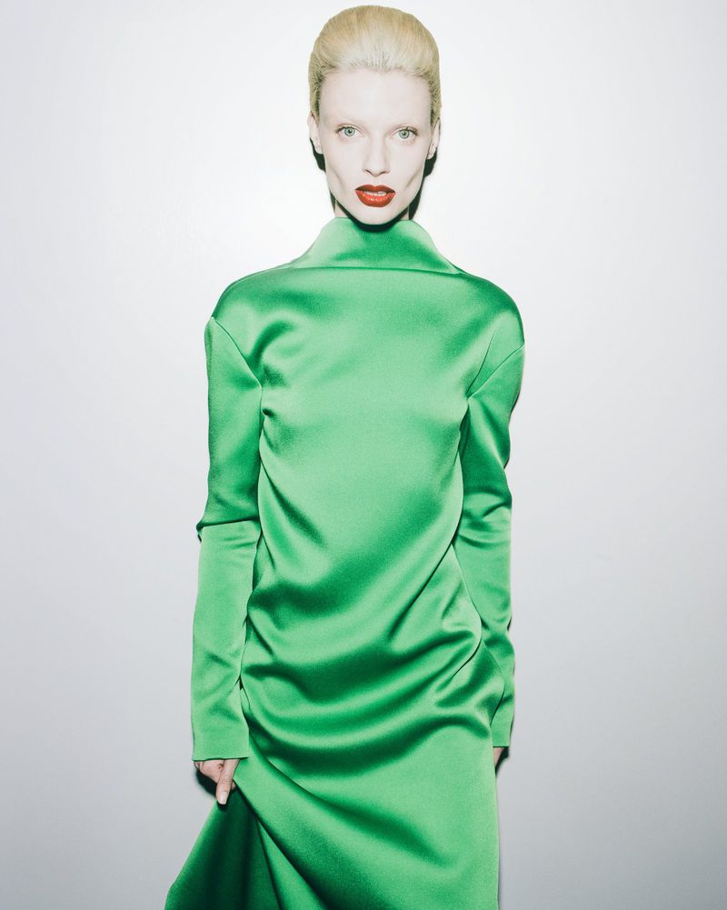Elegant woman in a vibrant green satin gown with high collar. The portrait is set against a bright white background.