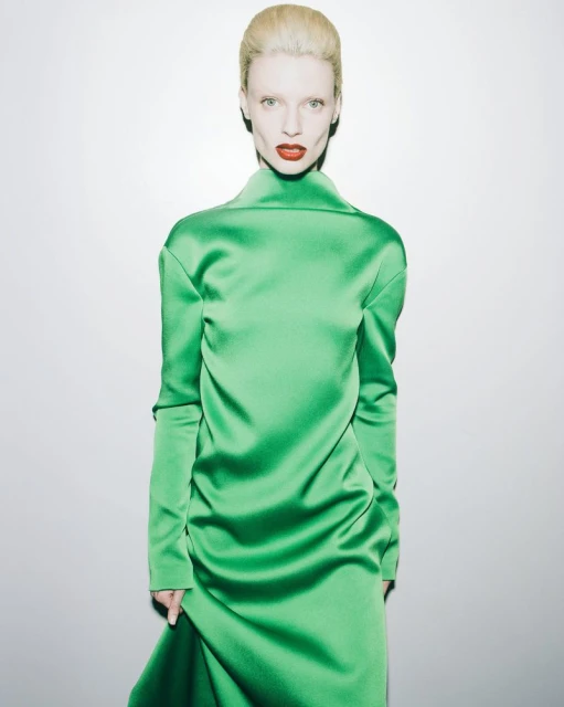Elegant woman in a vibrant green satin gown with high collar. The portrait is set against a bright white background.
